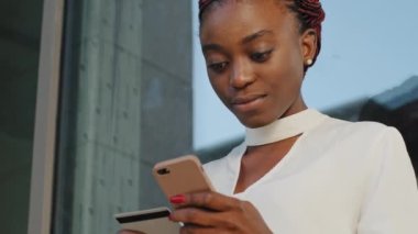 Afro-Amerikalı Afro-Amerikalı iş kadını kadın müşteri alıcısı cep telefonu akıllı telefonu kullanarak internet üzerinden alışveriş yapıyor ve banka kartı işlem emri için alışveriş uygulamasında ödeme yapıyor.