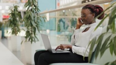 Genç Afro-Amerikan kadın serbest çalışan Afro-Afrikalı kız alışveriş merkezinin ofisindeki koltukta oturmuş cep telefonuyla konuşuyor.