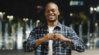 Afro-Amerikalı Afrikalı bir adam gece kentinde sevgi dolu romantik bir portrede kameraya bakarak kalbi parmaklarıyla şekillendiriyor. Sevgi ve şefkat gösteren sevimli çocuk. Şefkat destek işareti.