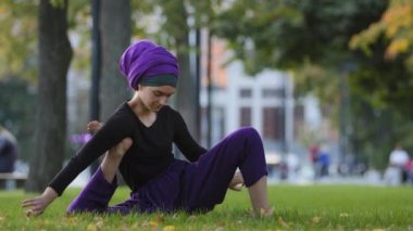 Kız tesettürlü müslüman kadın sporcu kadın Yogi çimenlerin üzerinde oturmuş, ayak altında el ele tutuşuyor, yoga antrenmanı yapıyor açık havada spor egzersizleri yapıyor.