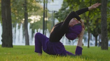 Müslüman İslami kız tesettür eğitmeni Guru yoga ustası kadın yeşil çimenlerin üzerinde egzersiz yapıyor spor yapıyor güzel akrobatik pozlar veriyor Asana çimenlikte arka kıvrımlı açık havada çimlerde oturuyor