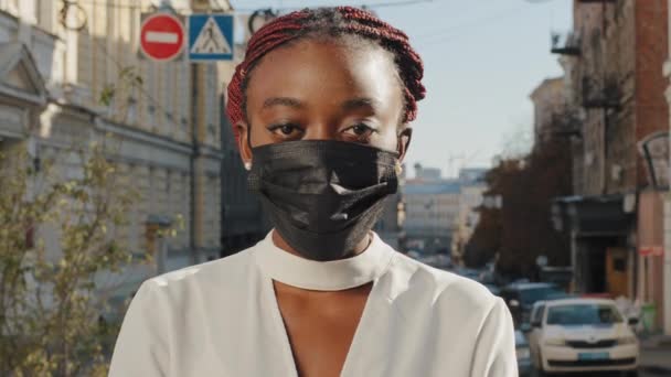 Женский портрет на открытом воздухе на городском фоне серьезное лицо афро-американская женщина африканская девушка юная клиентка покупатель студент туристические стенды, глядя на камеру носит медицинскую черную маску коронавируса пандемии — стоковое видео