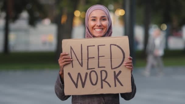 Ευτυχισμένη μουσουλμάνα γυναίκα στο χιτζάμπ στέκεται σε εξωτερικούς χώρους ισλαμικό αραβικό κορίτσι χαμογελώντας άνεργη αραβίδα γυναίκα χαιρετώντας χαιρετισμό δείχνοντας με το δάχτυλο σε χαρτόνι πανό χρειάζονται εργασία, απόλυση κρίση — Αρχείο Βίντεο