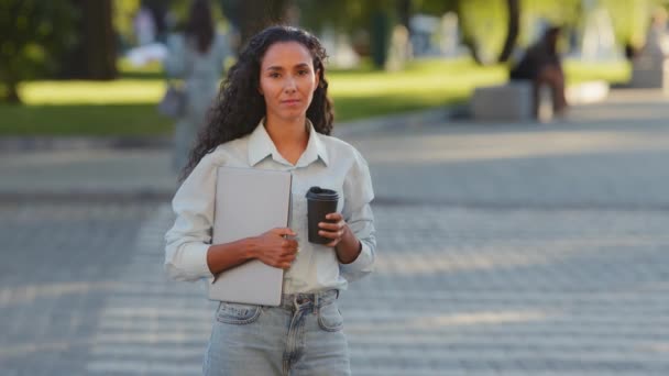 Succesvolle jonge Latijnse zakenvrouw meisje student stijlvolle dame staat in de stad straat crosswalk weg verkeer auto voetgangers kruising achtergrond met laptop en koffie kijken naar camera drinken thee — Stockvideo