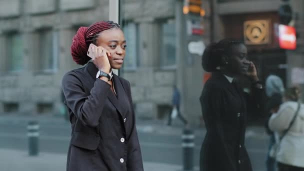 Mujer de negocios afroamericana hablando teléfono móvil ir a la oficina al aire libre. Chica afro joven serio empresario usando teléfono inteligente dispositivo de aplicación digital contestar llamada caminando llamando en la calle de la ciudad — Vídeo de stock