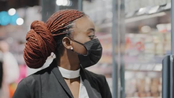 Портрет крупным планом Африканский женский медицинская маска девушка потребитель женщина покупатель смотрит на витрины магазинов, выбирая продукты питания выбирает товары в продуктовом магазине супермаркета в ковид блокировки карантина — стоковое видео