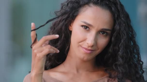 Portret kobiety uwodzicielski twarz sexy lady kaukaski millennial młoda brunetka dziewczyna z długimi kręconymi włosami skręcić na palec flirt patrząc w aparat, atrakcyjny wyraz twarzy na zewnątrz w mieście — Wideo stockowe