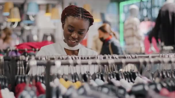 Afro-americana mulher africana menina comprador preto consumidor comprador sem máscara médica em loja local público loja escolher roupas corre em rack de bens vestidos comprando no shopping center. Descontos de venda — Vídeo de Stock