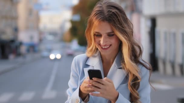 Portret gelukkig Kaukasisch meisje zakenvrouw op zoek naar mobiele telefoon verheugt overwinning goed nieuws chatten in het net ontvangt bericht van vriendje succesvolle e-commerce kopen online staande op de stad — Stockvideo