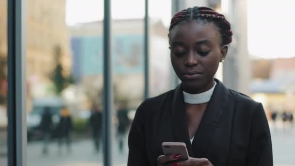 Portrait de jeune fille afro-américaine sérieuse succès professionnel femme d'affaires afro patron leader gestionnaire marche dans la rue de la ville en regardant dans le téléphone mobile bavarder en utilisant le travail en ligne smartphone — Video