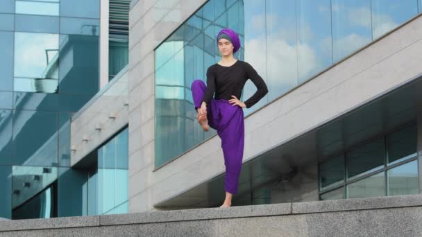 Mujer musulmana fuerte en hijab chica joven flexible estiramiento yogui yoga entrenamiento árbol pose asana hembra plantea pierna en el aire haciendo split estirar un pie equilibrio de pie ciudad edificio urbano fondo — Vídeos de Stock