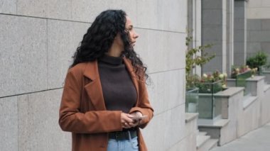 Genç İspanyol asıllı güzel iş kadını cep telefonuyla etrafa bakıyor. Taksi bekleyen birini gözetliyor. Bekleme randevusu.