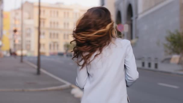 Powrót widok portret młoda piękna blondynka kaukaska pani z wspaniały kręcone długie włosy stylowa fryzura obracając się wokół patrząc na aparat skręca loki latające w powietrzu kobieta dziewczyna model pozowanie miasto ulica — Wideo stockowe