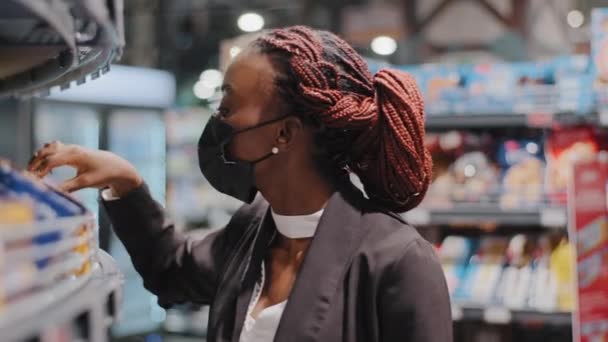 Close-up afrikaanse amerikaanse vrouw meisje consument vrouwelijke shopper draagt gezicht medisch masker picks goederen in supermarkt supermarkt maakt keuzes kopen van voedsel in winkel covid lockdown quarantaine pandemie — Stockvideo