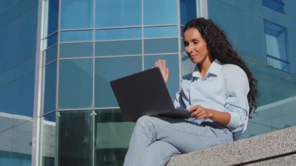 Młoda uczennica korzystająca z laptopa siedząca w mieście. Piękny biznes kobieta z komputerem o online video czat zdalny odległa rozmowa mówi machając cześć siedzieć na ulicy ait pocałunek gest — Wideo stockowe