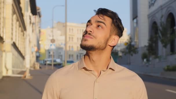 Retrato de feliz inspirado calma sozinho árabe latino homem de negócios terist barbudo cara em pé na cidade nova urbano fundo edifícios pensando sonhando desfrutar de rua vista ar fresco olhando para o céu — Vídeo de Stock