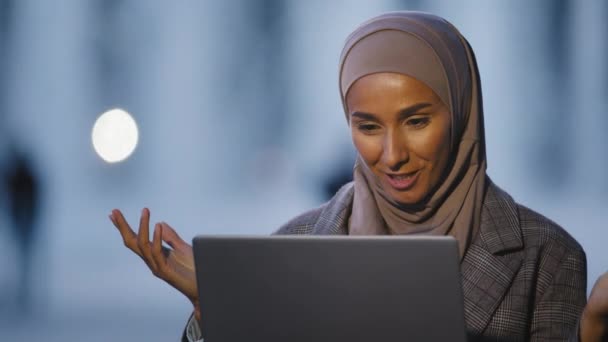 Porträtt arabiska islamiska muslimska affärskvinna flicka internationell student talar video chatt konferens med bärbar dator talar i webbkamera sitter på kvällen på gatan i staden fjärrsamtal — Stockvideo