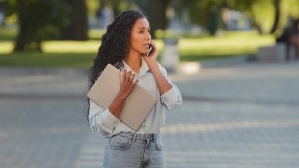 ノートパソコンを持つ若い女の子のビジネスの女性は、道路の背景を横断歩道上の街に立って電話タクシーを呼び出す呼び出しに答える携帯電話で話すリモート会話の交渉 — ストック動画