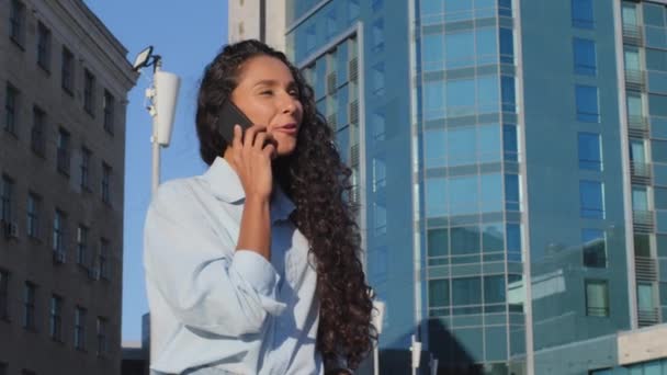 Mulher de negócios jovem bonita falando no telefone celular com amigo negociações distantes com colegas ao ar livre close-up. Menina estudante cliente faz pedido on-line usando o fundo do edifício do smartphone — Vídeo de Stock