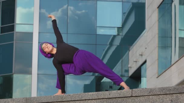 Donna forte in hijab ragazza flessibile facendo esercizi di yoga su strada città costruzione sfondo sport signora si trova in tavola laterale su una mano si estende corpo in piedi in spago stretching acrobatica pratica — Video Stock