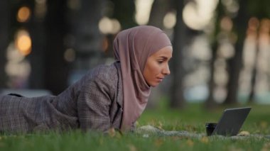Müslüman odaklı, tesettürlü, tesettürlü, internetten çalışan, çim yeşili çimlerde okuyan, kahve içip sohbet eden, kablosuz bilgisayar uygulaması kullanan, İslamcı kız iş kadını.