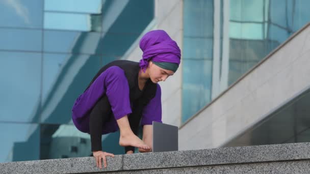 Jovem mulher de negócios forte islâmico muçulmano estudante está em equilíbrio suporte asana movimento acrobático digitando com os pés no laptop edifício da cidade fundo fecha computador acabamento trabalho descansando — Vídeo de Stock