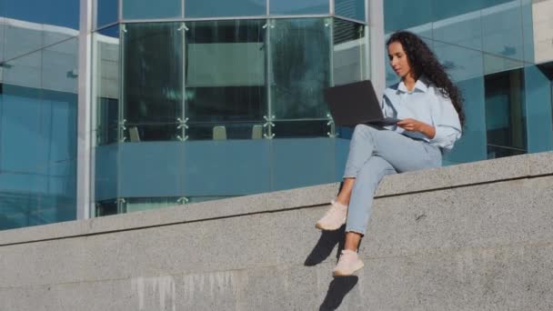 Jovem estudante bem sucedido mulher de negócios usuário distante trabalha on-line remoto e-learning com laptop na cidade. Cliente feminino com computador de compras no serviço de aplicativo de internet sentado edifício fundo — Vídeo de Stock