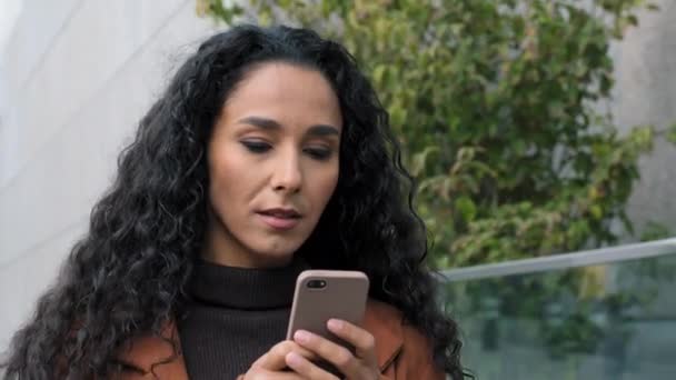 女性の肖像画顔深刻なラテンヒスパニック系の女の子若いビジネス女性が街でスマートフォンの女性と一緒に路上で歩く携帯電話のブラウジングチャットオンライン受信メッセージでガジェットデバイス — ストック動画