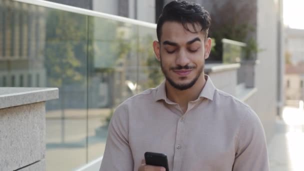 Retrato satisfecho latino árabe barbudo guapo exitoso hombre de negocios chico caminando calle cerca del edificio de la empresa creativa oficina mirando en el teléfono móvil chat en el teléfono inteligente contestando mensaje — Vídeos de Stock