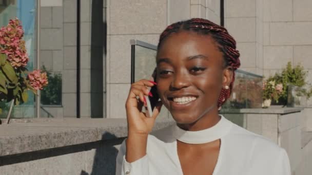 Жіночий портрет щаслива весела усміхнена дівчина афроамериканська бізнес-леді, що ходить по вулиці міста, розмовляє на мобільному телефоні, відповідаючи на дзвінки в чаті з друзями на смартфоні бездротовий гаджет — стокове відео