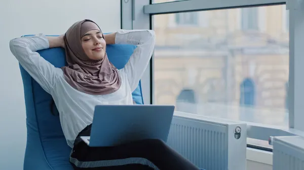 Avslappnad vacker muslimsk arabisk affärskvinna arbetare sitter i bekväm fåtölj meditera, positiv lugn arabisk kvinna koppla hålla handen bakom huvudet dröm vila från datorn sträcka känna sinnesfrid — Stockfoto
