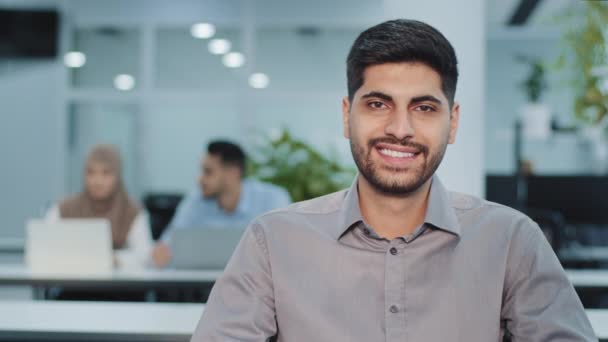 幸せなアラブの起業家の若い男性トップマネージャーの肖像画を確信しています。笑顔の会社の所有者、起業家、リーダー、カメラを見て成功した従業員。部下が背後で働いてる — ストック動画