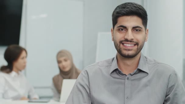 Portré fiatal mosolygós arab vállalkozó sikeres üzletember, miután diadal a találkozón, épített birodalom, felső menedzser nagy tapasztalattal. Különböző beosztottjai dolgoznak a háttérben. — Stock videók
