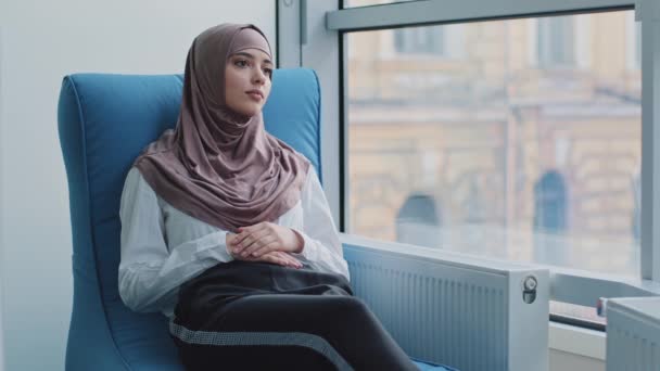 Estudiante interna árabe en hijab a la espera de examen o resultados de la entrevista en sillón. Candidato de trabajo se sienta en la oficina de agente de reclutamiento esperando reunión con el empleador para la contratación. HR, concepto de carrera — Vídeos de Stock
