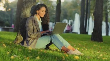 Genç kız öğrenci başarılı iş kadını müşteri kullanıcısı Park City 'de çimlerin üzerinde oturuyor açık havada internette internet üzerinden laptop bilgisayar uygulaması e-öğrenme alışverişi yapıyor.