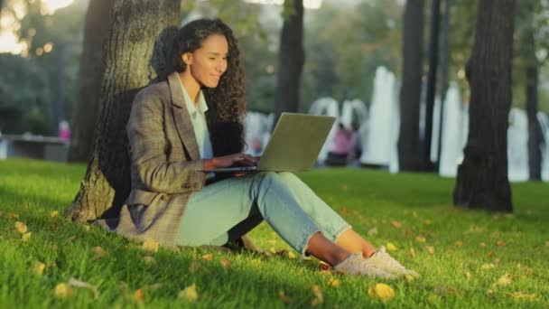 Joven estudiante exitosa mujer de negocios cliente usuario sentado en césped verde hierba en el parque de la ciudad al aire libre trabajando en línea en red utilizando el ordenador portátil aplicación e-learning compras en Internet — Vídeo de stock