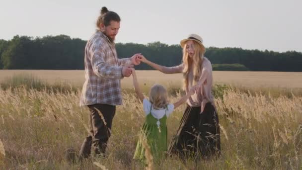 Famille heureuse s'amuser à l'extérieur en tenant la main en jouant dans le champ de blé. Concept d'enfance. Jeune mère au chapeau, père barbu avec petite fille enfant danse en cercle en s'amusant dans la nature ensemble — Video