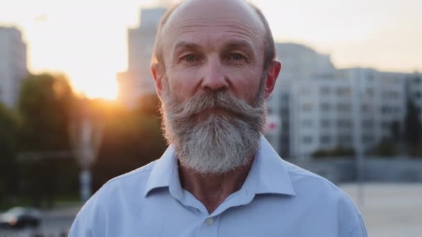 Viejo abuelo guapo con barba gris y bigote posando solo en la ciudad. Elegante hombre de edad de jubilación en camisa mirando seriamente a la cámara. Atractivo anciano cara masculina primer plano retrato al aire libre — Vídeo de stock