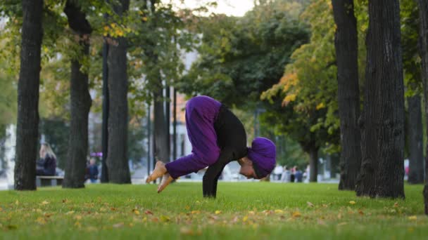 Professora muçulmana feminina em hijab prática ioga poder de fluxo asana no parque da cidade no treino de grama para corpo saudável forte coluna postura movimento de pernas atléticas no ar. Mulher menina sentir energia formação bakasana — Vídeo de Stock