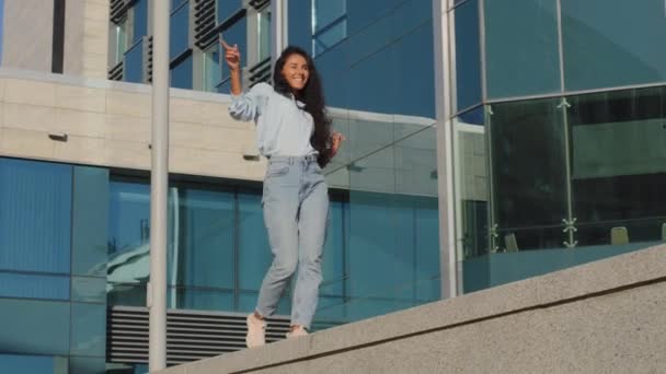 Aktivní veselá bezstarostná mladá dívka žena v ležérní oblečení s dlouhými kudrnaté černé vlasy jít tancovat pohybující se aktivně pohyb s rukama tanec bavte krok na terase v budově města pozadí — Stock video