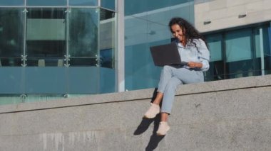 Gülümseyen mutlu genç iş kadını serbest çalışan kız sokak kenti binasında kablosuz bilgisayarla internetten alışveriş yaparak iyi bir teklif fırsatı elde ediyor.