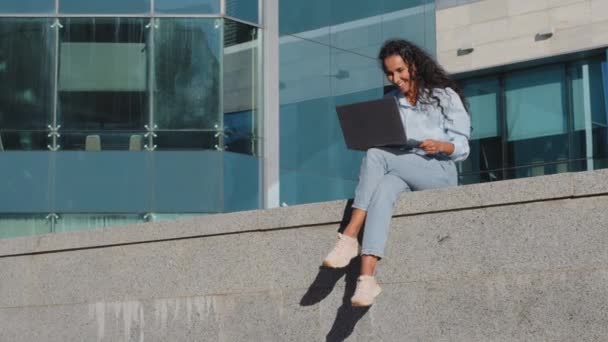 Largo tiro sonriendo feliz joven mujer de negocios freelancer chica estudiante sentado en la calle ciudad edificio fondo con el ordenador portátil inalámbrico trabajando estudiar compras en línea obtiene buena oportunidad de aviso oferta — Vídeos de Stock