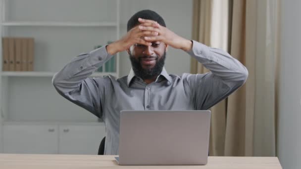 Zaostřený mladý vousatý zaměstnanec kanceláře černého podnikatele, píšící na notebooku, dal ruce za hlavu, aby si odpočinul od práce s počítačem. Nadechněte se čerstvého klimatizovaného vzduchu uvnitř moderní místnosti — Stock video