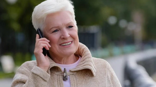 Blonde Frau der 60er Jahre telefoniert mit Freundin im Freien und unterhält sich angenehm distanziert mit erwachsenen Kindern, älteren Generationen und modernen Technologien — Stockfoto