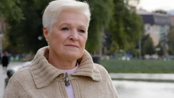 Primer plano retrato triste seria atractiva mujer benevolente de la edad de jubilación. Calma señora madura que medita en ropa casual con el pelo corto gris peinado elegante de pie posando al aire libre mirando a un lado — Foto de Stock