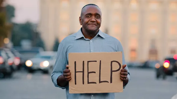 Unhappy black African American businessman holding cardboard with text help emotional pointing on sign. Stressed frustrated man hold poster looking for job during pandemic talks about himself outdoor — Stock Photo, Image