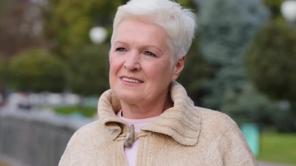 Primer plano retrato sonriendo señora madura en ropa casual posando al aire libre mirando a un lado gira la cabeza a la cámara. Calma atractiva mujer benevolente de la edad de jubilación con el pelo corto con estilo gris — Vídeos de Stock