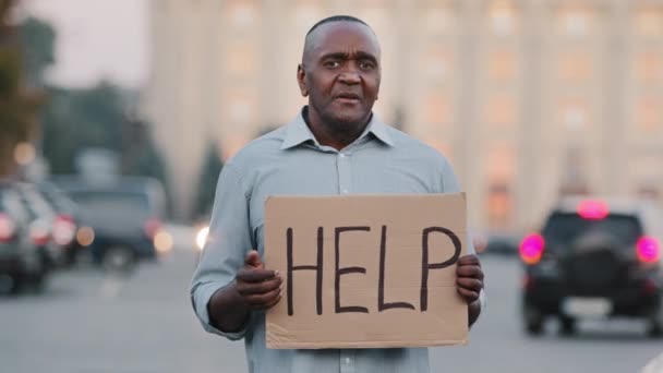 Triste estresado frustrado anciano afroamericano pobre hombre edad de jubilación, turista perdido, sosteniendo pancarta de cartón con inscripción necesita ayuda pide dinero crisis problemas de salud durante la pandemia covid — Vídeos de Stock