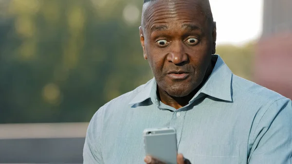 Worried nervous african man holding cell phone frustrated by problem having complaints on bad service, angry black person annoyed with mobile app error spam message on slow stuck broken smartphone — Stock Photo, Image