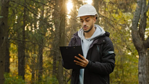 Joven hombre indio experimentado ingeniero forestal en hardhat con tabletas que toman medidas para la reforestación de bosques. Trabajando y supervisando en el parque, observando el santuario de vida silvestre revisando árboles —  Fotos de Stock